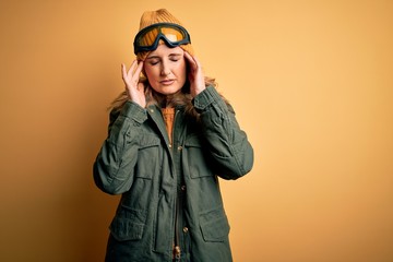 Middle age beautiful blonde skier woman wearing snow sportwear and ski goggles with hand on headache because stress. Suffering migraine.