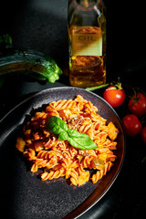 Chickpeas fusilli with cherry tomatoes, zucchini, linseed and olive oil, on a black background with direct sunlight on the pasta
