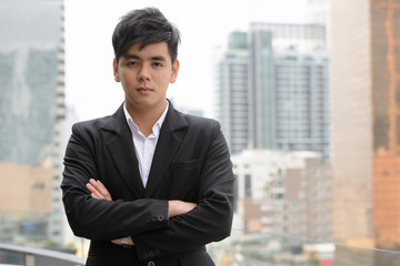 Portrait of young handsome Asian businessman with arms crossed in the city