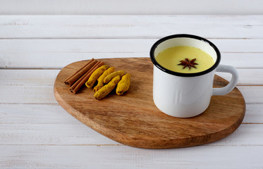 Cup of turmeric golden milk served with spices –cinnamon and star anise on white wooden background.