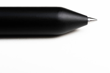 A macro shot of the writing tip with a portion of the barrel of a streamlined modern black ballpoint pen set on white background.