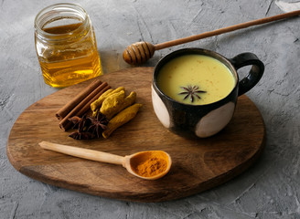 Cup of turmeric golden milk served with honey and spices –cinnamon, star anise on grey concrete background.
