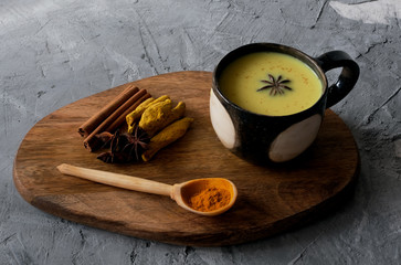 Cup of turmeric golden milk served with spices –cinnamon and star anise on grey concrete background.