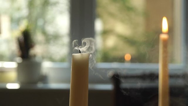 female mouth blowing out candle, closeup of young woman's lips extinguishing candle in foreground, blurred candle burning in background, rising smoke of blown out candle