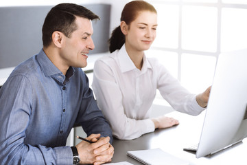 Friendly smiling businessman and woman working with computer in modern office. Headshot at meeting or workplace. Teamwork, partnership and business concept