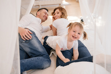 Cute kid daughter and dad tickling mom having fun good time playing together at home, happy parents and little child girl enjoying funny activity and communication, family laughing relaxing