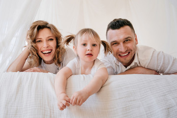 Cute kid daughter and dad tickling mom having fun good time playing together at home, happy parents and little child girl enjoying funny activity and communication, family laughing relaxing