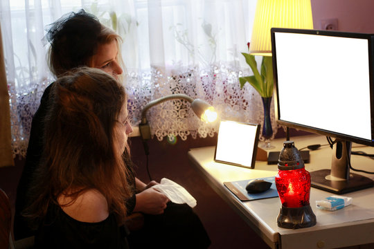 Young women in mourning are looking on computer screen. Computer set with snitch and picture frame template. Sad girls in black are watching funeral live stream. 