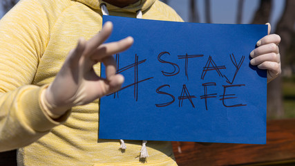 Stay safe sign on blue chroma key paper held by a man in surgical gloves giving ok sign with hand