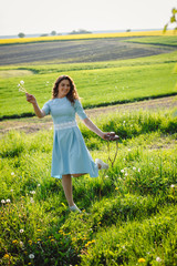 Beautiful young woman on a field background blowing a dandelion. Healthy smiling girl on green nature background. Allergy-free concept. The beautiful girl outdoors enjoys nature, lives.