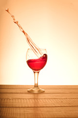 A small glass of red wine with splashes in the orange background