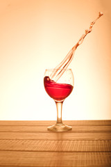 A small glass of red wine with splashes in the orange background