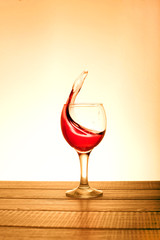 A small glass of red wine with splashes on wooden table on a sunny background