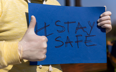 Stay safe sign on blue chroma key paper held by a man in surgical gloves pointing thumbs up