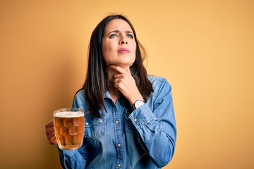 Young woman with blue eyes drinking jar of beer standing over isolated yellow background Touching painful neck, sore throat for flu, clod and infection