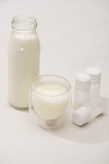 High angle view of bottle and glass of homemade yogurt near containers with starter cultures on white