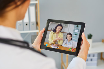 Doctor online. A female doctor therapist is looking at the screen of a tablet while the family is...