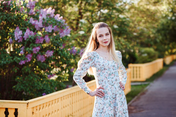 Beautiful woman is spending time outdoors in the village, in the countryside. Lilac alley in the background. 