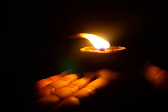 Lit diya or clay lamp on the palm of a person
