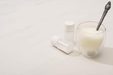 High angle view of glass of homemade yogurt and teaspoon near containers with starter cultures on white