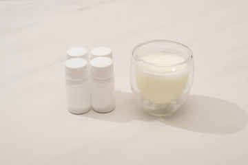 Glass of homemade yogurt near containers with starter cultures on white background