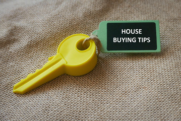 A yellow toy key with a wooden tag written with House Buying Tips on a rugs background.