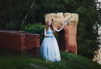 beautiful red-haired girl walks with an owl on her hand against the background of the castle