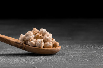Side view on raw uncooked chickpeas in the wooden spoon on the grey background, horizontal format