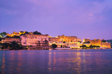 Fototapeta premium View of famous romantic luxury Rajasthan indian tourist landmark - Udaipur City Palace in the evening twilight with dramatic sky - panoramic view. Udaipur, India