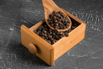 Fototapeta na wymiar Side view closeup on black fragrant peppercorns in the small wooden box and wooden spoon on the grey background, horizontal format