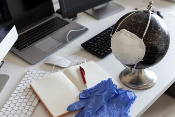 Medical mask put on a globe and gloves on the desk. Work and study at a distance. Desk, work space for working at home. Office background