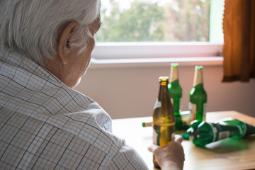 old senior man sit next to table drink alcohol bottle at home sad and alone