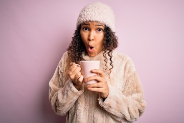 Young beautiful woman with curly hair drinking mug of coffee over isolated pink background scared in shock with a surprise face, afraid and excited with fear expression
