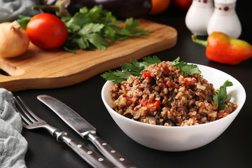 Healthy buckwheat cooked with vegetables in a white bowl on a dark background, Horizontal format, Closeup