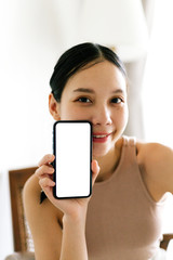 Asian cute woman is showing white blank smartphone screen on home studio background