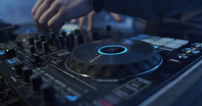 DJ plays live set and mixing music on turntable console at stage in the night club. Disc Jokey Hands on a sound mixer station at club party. DJ mixer controller panel for playing music and partying.