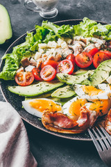 Cobb salad with chicken, avocado, tomatoes, eggs, bacon and cheese with sauce on a black  table close up.