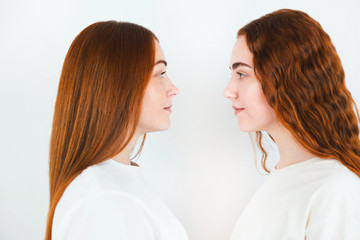 portrait of two redheaded young women looking at each other standing sideways on isolated white backgroung, close up