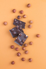 Pieces of dark chocolate with hazelnuts on the light brown background. Closeup. Location vertical