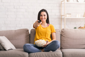 Stay home entertainments. Lovely girl with popcorn watching TV on sofa in living room