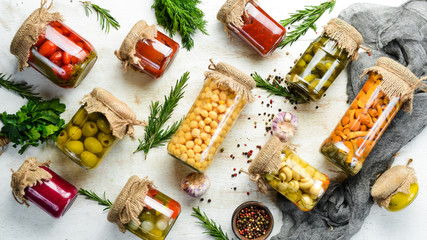 Canned food in glass jars on white wooden background. Pickled vegetables and mushrooms.