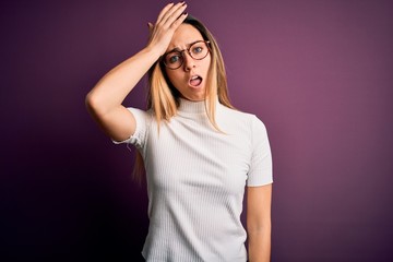 Young beautiful blonde woman with blue eyes wearing casual t-shirt over purple background surprised...