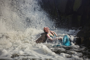 beautiful red-haired girl bathes in a stormy stream of a waterfall, hot summer