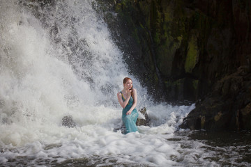 beautiful red-haired girl bathes in a stormy stream of a waterfall, hot summer