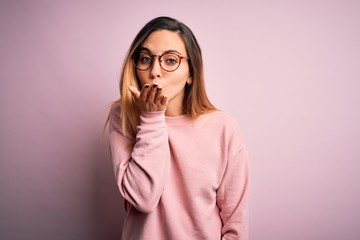 Beautiful blonde woman with blue eyes wearing sweater and glasses over pink background looking at the camera blowing a kiss with hand on air being lovely and sexy. Love expression.