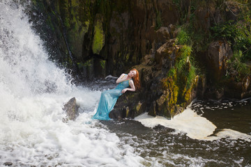beautiful red-haired girl bathes in a stormy stream of a waterfall, hot summer