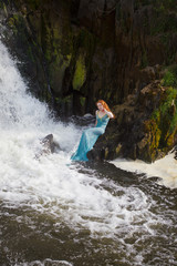 beautiful red-haired girl bathes in a stormy stream of a waterfall, hot summer