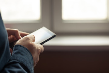 Man holding cell phone in his hands near a window. Close up with selective focus on right hand