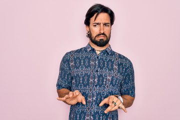 Young handsome hispanic bohemian man wearing hippie style over pink background disgusted expression, displeased and fearful doing disgust face because aversion reaction.