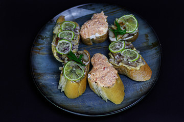 Toast bread with lime, fish paste. Restaurant dish on a big plate on black background.